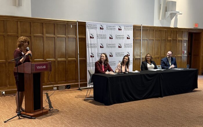 woman standing at podium with a panel of speakers at the right