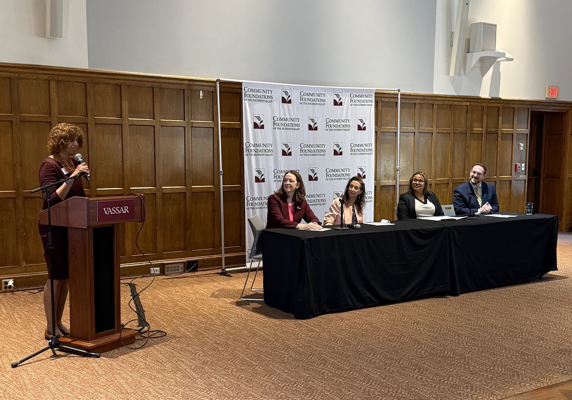 woman standing at podium with a panel of speakers at the right