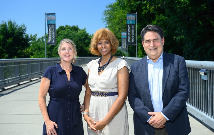 photo of three people standing on a bridge with trees in the background