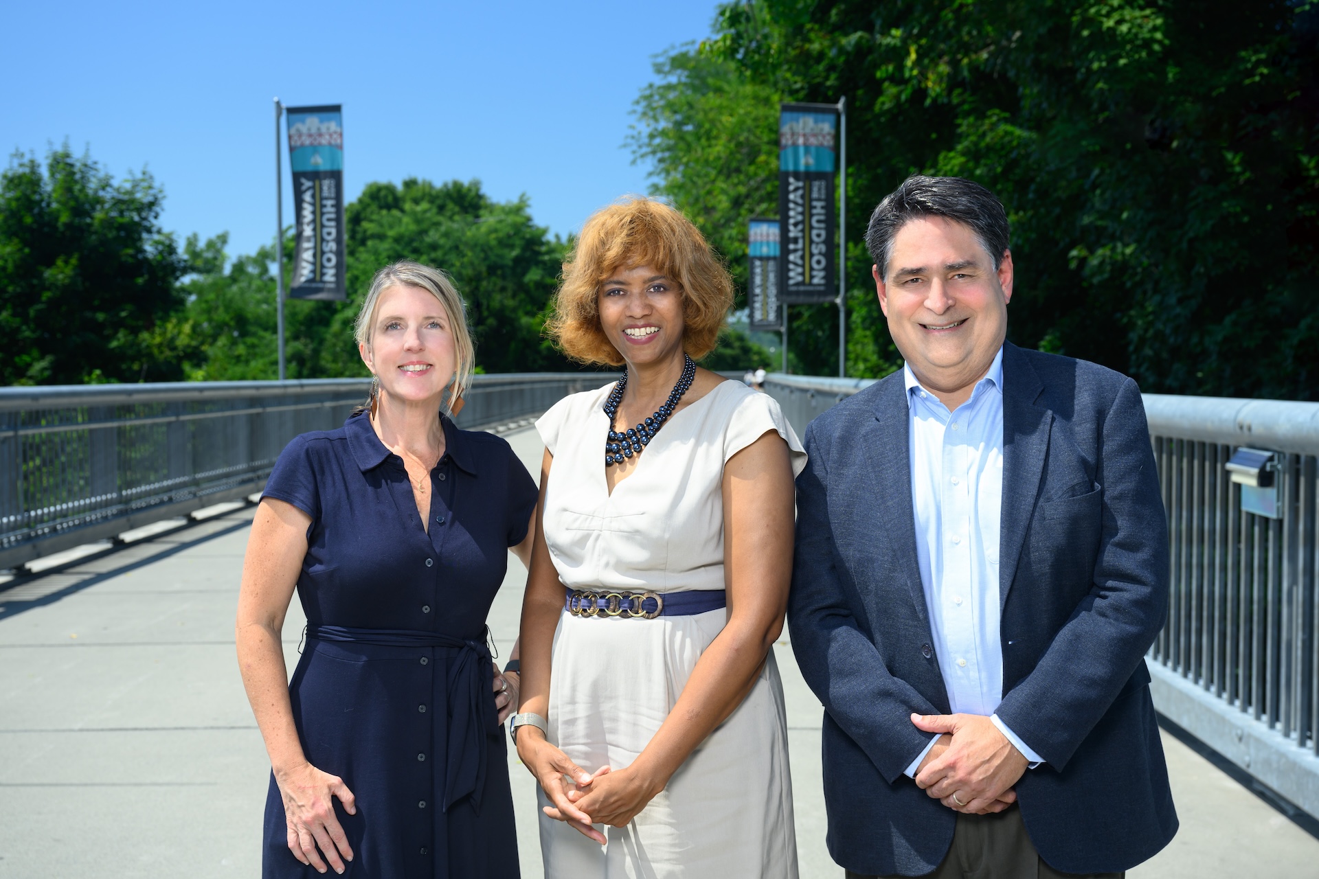 photo of three people standing on a bridge with trees in the background